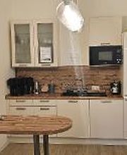 Küche mit mehreren Schränken, Wasserkocher, Kaffeemaschine und Spüle. Davor ein Tisch.