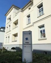 Beschilderung WBS TRAINING vor gelbem Haus.