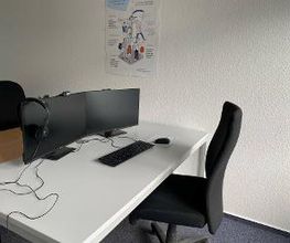 Arbeitsplatz mit zwei Bildschirmen, Tastatur, Maus und Headset sowie einem schwarzen Bürostuhl.