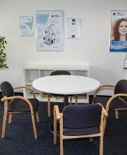 Beratungszimmer. Ein runder Tisch mit vier Stühlen. Im Hintergrund steht eine grüne Zimmerpflanzen und es hängen verschiedene Plakate an der Wand.