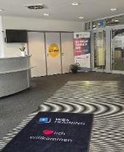 Eingangsbereich mit Empfang, Wartebereich, Werbeaufsteller und einer großen, grünen Zimmerpflanze. Auf dem Boden liegt ein Teppich mit der Aufschrift „WBS TRAINING – Herzlich Willkommen“
