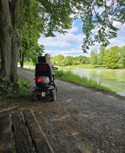 Selbstbestimmt unterwegs trotz Unterstützungsbedarf: Eine Seniorin genießt mit ihrem Elektromobil einen Ausflug am Wasser. Persönliche Betreuung kann dabei helfen, Mobilität, soziale Teilhabe und vertraute Aktivitäten im Alltag zu erhalten.