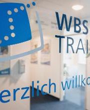 Eingangstür aus Glas mit Blick in den Flur. Auf der Tür ein blauer Schriftzug WBS TRAINING – Herzlich willkommen plus Logo. 