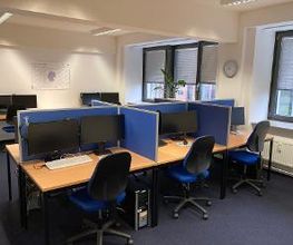 Schulungsraum mit mehreren Arbeitsplätzen mit jeweils 2 Bildschirmen, einem Bürostuhl, Tastatur, Maus und Headset.