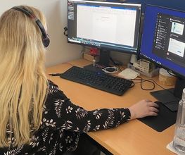 Eine Teilnehmerin sitzt an ihrem Arbeitsplatz vor 2 PC-Bildschirm und trägt ein Headset.