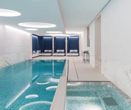 Indoor swimming pool with sleek modern design, white marble walls, and lounge chairs at The Woodward Geneva.