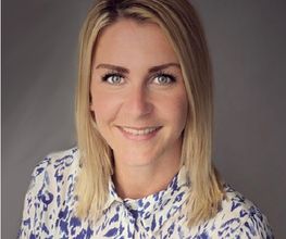 Frau mit blonden, mittellangen Haaren und weißer Bluse mit blauen Streifen.