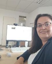 Eine Frau mit Brille sitzt an einem PC und dreht sich für das Foto um.