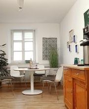 Gemütliche Küche mit Sitzecke, Kaffeemaschine und Zimmerpflanze. An der Wand hängt eine grüne Tafel.
