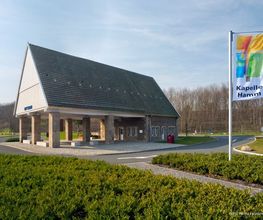 Auch in den Außenanlagen begegnet die Kapelle dem Verkehr der Autobahn mit Ruhe. Die Skulptur, ein Wassersprudelbecken und verschiedene Sitzgelegenheiten lassen den Aufenthalt zur Entspannung werden.
Westlich der Kirche steht eine Stahlskulptur von dem Soester Künstler Michael Düchting. Sie trägt den Titel "Das Tor". Es handelt sich um eine sechs Meter hohe und rund 7,5 Tonnen schwere Plastik aus Stahlplatten mit einem schmalen Durchgang in der Mitte. Der Bildhauer beschreibt sein Kunstwerk als Metapher für die aktuelle Reise wie auch für das unterwegs Sein im Leben.