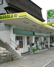 AGROLA Tankstelle in Rüegsbach, bei Autogarage; leicht gebogenes Dach mit Logo-Schild angebracht, zwei Tanksäulen, rechts Autogarage, links Treppe zu Wohnhaus