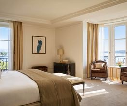 Spacious bedroom with king bed, French windows, and soft beige decor at The Woodward Geneva.