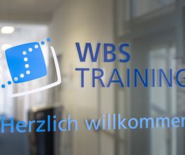 Eingangstür aus Glas im Treppenhaus mit der Aufschrift WBS TRAINING. Herzlich Willkommen.