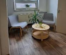 Kleiner Pausenraum mit 2 Sesseln und einem Beistelltisch mit Deko. Im Hintergrund ein großes Fenster und eine Zimmerpflanze.