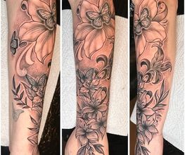 Filigranes Blackwork-Tattoo mit großen Blüten, Schmetterlingen, Blättern und Ornamenten als florales Unterarm-Motiv.
