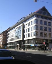 Ein vierstöckiges, weißes Gebäude mit Spitzdach an einer Straßenkreuzung.