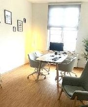 Beratungsraum mit Parkettfußboden, hellen Holzmöbeln, Clubsesseln und Kindermalecke