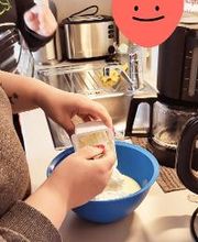 Eine Teilnehmerin beim Backen am Standort. Schüssel mit Mehl. Darüber ein Herz mit einem lächelnden Gesicht.