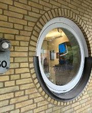 Außenansicht des runden Fensters mit blauem WBS TRAINING Logo. Links daneben befiundet sich ein Schild mit einer Lampe und der Nummer 50 als Aufschrift.