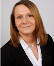 Portrait einer Mitarbeiterin mit Schulterlangen Haaren, im Business Look. Sie lächelt freundlich in die Kamera.