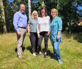 Ein Gruppenbild vom Standortteam. 4 Personen stehen an einem sonnigen Tag draußen im Grünen.