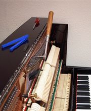 Klavier in geöffnetem Zustand mit Stimmhammer und Werkzeug. Darstellung des Prozesses der Klavierstimmung für einen reinen und harmonischen Klang.