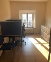 Ein Schulungsraum mit zwei Arbeitsplätzen und einem Regal auf der rechten Seite. Durch ein Fenster gelangen Sonnenstrahlen in den Raum.