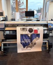 mediaService Bremen | Full-Stack Werbeagentur - Ein professioneller Roland VersaCAMM Plotter und Großformatdrucker druckt ein großes Ausstellungsplakat in einer hellen Druckwerkstatt.
