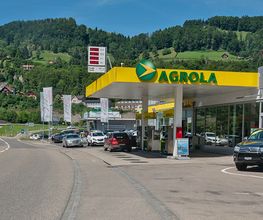 AGROLA Tankstelle und LAVEBA Shop in Wattwil bei Autogarage; direkt an Strasse; grosse digitale Preisanzeige über Tankstellen-Dach; Autos an Strasse geparkt