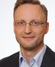 Portrait eines Mitarbeiters mit Brille, der freundlich in die Kamera schaut.