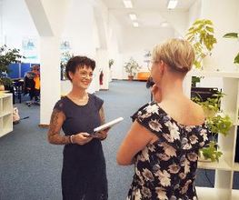 Zwei Frauen im Gespräch. Die Bildnähere steht mit dem Rücken zur Kamera.