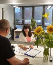 2 Kolleg:innen unterhalten sich über Formulare. Auf dem Tisch steht eine Vase mit Sonnenblumen.