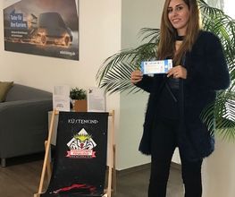 Eine Frau steht neben einem Strandstuhl und hält eine Eintrittskarte in der Hand. Gewinnspiel für Umschüler "Eishockeykarten"