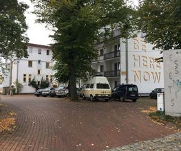 Außenansicht vom Gebäude mit einigen Bäumen und Autos davor.