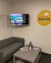 Pausenraum mit grauem Sofa und einem Tisch. In der Ecke hängt ein Bildschirm an der Wand.