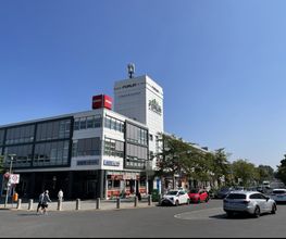 Gebäude an einer Straße mit parkenden Autos und Bäumen. Auf dem Gebäude ein Schild von Penny.