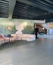 Aufenthaltsbereich vielen Sitzmöglichkeiten, großes florales  Bild mit Kopfmotiv, im Hintergrund stehen Schreibtische und Sitzsäcke 