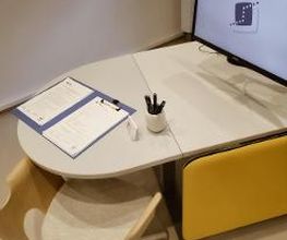 Blick auf einen im Beratungsraum. Auf dem Tisch steht ein Computer-Monitor mit WBS TRAINING Logo als Bildschrimschoner  sowie ein Klemmbrett mit Dokumenten.