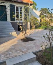 Individuell gestaltete Natursteinterrasse mit integrierter Pflanzinsel und neu angelegter Treppe. KK GaLaBau bei Berlin verbindet bei diesem Projekt moderne Pflasterarbeiten mit bestehenden Gehölzen und der Architektur des Hauses.