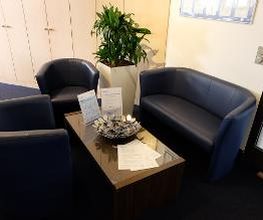 Sitzgruppe bestehend aus 2 blauen Sesseln und einem Sofa. Ein Beistelltisch mit Süßigkeiten, dahinter eine Topfpflanze und mehrere Schränke.