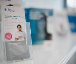 Nahaufnahme eines Werbeprospekte-Aufsteller. Im Hintergrund befinden sich weitere Informationsmaterialien.