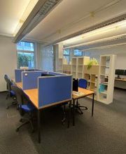 Schulungsraum mit mehreren Arbeitsplätzen mit Bürostühlen und blauen Trennwänden. Im Hintergrund ein Regal mit Pflanzen als Raumtrenner.