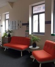 Wartebereich mit zwei roten Sofas und Grünpflanzen.