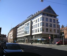 Ein vierstöckiges, weißes Gebäude mit Spitzdach an einer Straßenkreuzung.