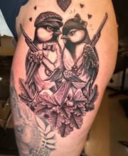 Detailreiches Black-and-Grey-Tattoo mit zwei verliebten Vögeln, Gewehren, Herzen und Eichenlaub auf dem Oberschenkel.