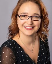 Frau mit Brille und mittellangen Haaren in schwarzer gepunkteter Bluse.