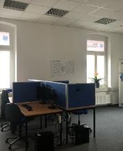 Schulungsraum mit mehreren Arbeitsplätzen mit jeweils 2 Bildschirmen, einem Bürostuhl, Tastatur, Maus und Headset. An der Wand ein Kalender.