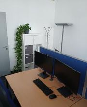 Schreibtisch im Trainingsraum mit zwei Bildschirmen, Tastatur und Maus. An der Wand steht ein Regal mit Pflanze