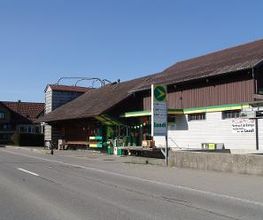 AGROLA Tankstelle in Waldkirch; bei Landwirtschaftsgebäude gelegen. Im Vordergrund Strasse und Totem mit Preisanzeige AGROLA Diskus und Landi Logo