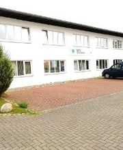 Zweistöckiges Schulungsgebäude WBS TRAINING in Waren. Davor ist ein Parkplatz mit einem geparkten AUto zu sehen.